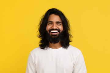 Emotional handsome millennial eastern guy laughing on yellow background