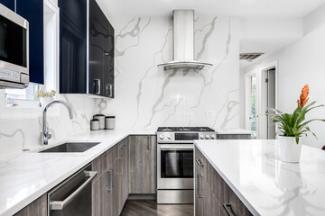 A modern kitchen detail with glossy blue and wood cabinets, stainless steel appliances, and a marble countertop and backsplash. No brands or logos.