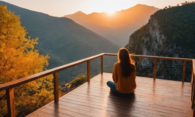 Picture from the back of a woman sitting on wooden porch extending into a high mountain cliff at...