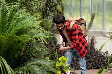Naklejka na ściany i meble Young dark-haired man making photos in botanical garden
