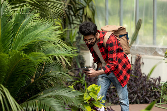 Young dark-haired man making photos in botanical garden