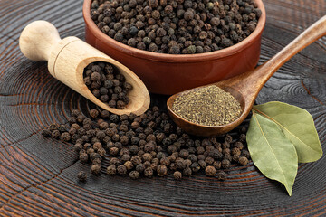 Wooden pepper mill, black peppercorns, ground black pepper and laurel leaves on old wooden table.