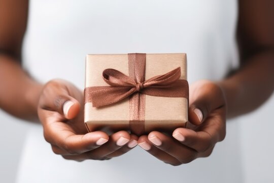 Delicate African American hands cradle a gift wrapped in earth toned paper and satin ribbon, conveying a sense of care and celebration