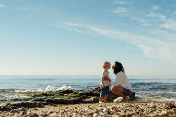 Mother plays with her baby on the beach. A woman with her son on the seashore. Mom kisses her son.