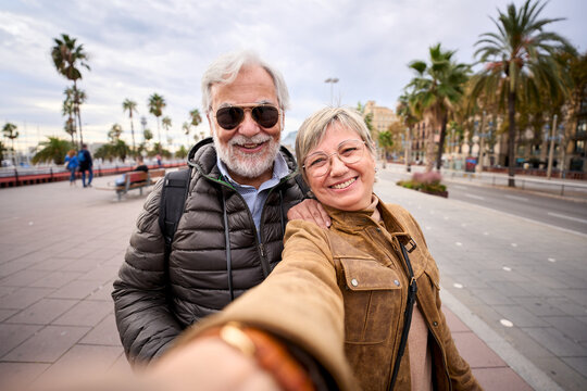 Happy Caucasian senior tourist couple take selfie together. Husband and wife love smiling looking at camera enjoying pensioner journeys in European city street. Older people retirees sightseeing 