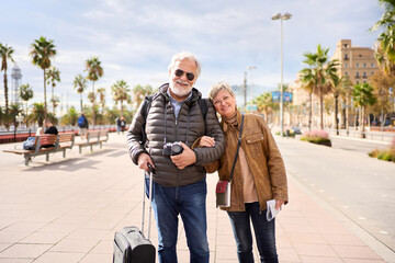 Smiling Caucasian mature tourist couple standing posing looking at the camera in the street with...