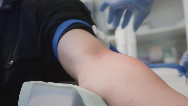 Nurse disinfects hand of male patient thoroughly preparing for medical procedure. Professional doctor in rubber gloves ties tourniquet to locate suitable vein for blood sample collection