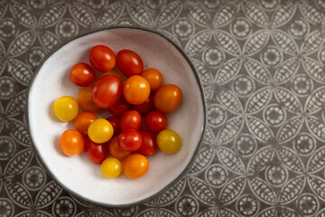 Top view of cherry tomatoes in a white bowl on a grey tray