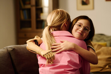 Happy affectionate girl with partial arm giving hug to her mother in pink shirt while sitting in...