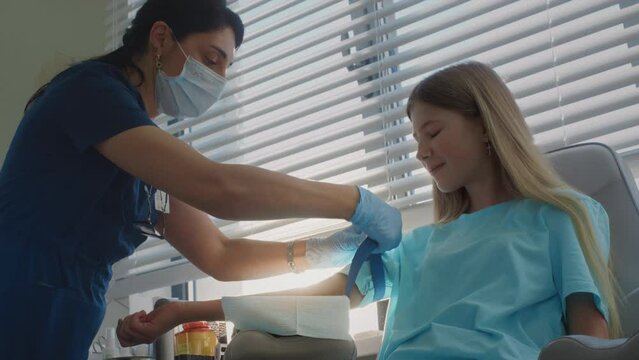 Nurse adjusts tourniquet carefully to make process comfortable for girl teenager patient. Professional doctor prepares area for upcoming blood draw maintaining cheerful atmosphere during procedure