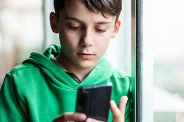Boy with smartphone indoors. Preteen boy using a phone checking social media. Concept of children...
