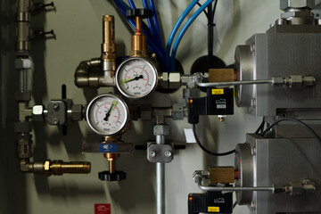Part of automated equipment with two mechanic meters, cables and metallic pipes installed inside large industrial plant or factory