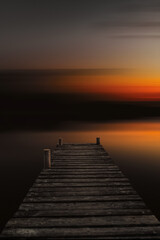Abstract lake landscape at sunset with an old wooden boardwalk. Dock in lake with abstract blurred background in dark sunset evening