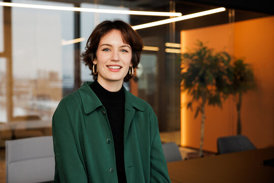 Confident young professional woman working in a modern office. Business trip woman posing for camera for business portraits in green shirt. A young marketing specialist inspired to work