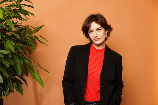Dynamic Professional Woman in Modern Office Setting. Businesswoman Posing for Portraits in Red Sweater and Black Jacket. Inspired Young Marketer at Work