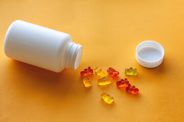 children's jelly vitamins in a bottle on a yellow background - obrazy, fototapety, plakaty