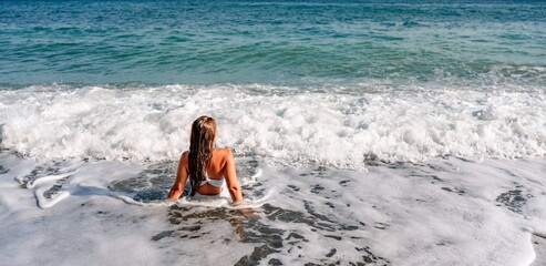 Happy woman in bikini sits on the sea beach. Tanned girl sunbathing on a beautiful shore. Summer vacation or holiday travel concept