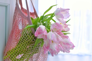 There are pink tulips in the string bag that hangs on the door handle.