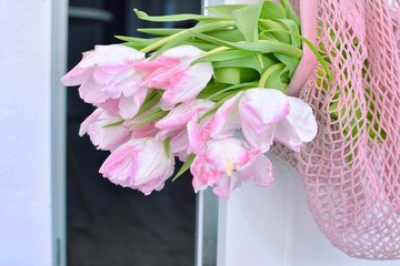There are pink tulips in the string bag that hangs on the door handle.