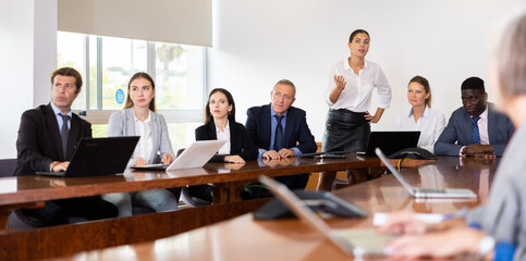 Multiracial group of mature and young businesspeople sitting around table and listening to...