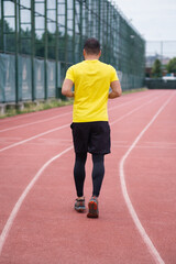 Obraz premium Active man in comfortable activewear jogs along the stadium track, healthy and active lifestyle backside view. 
