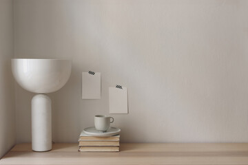Blank greeting cards mockups mockups taped on white wall. Elegant modern marble lamp, geometric shade. Wooden table, desk with old books and cup of coffee. Interior. Home office concept.
