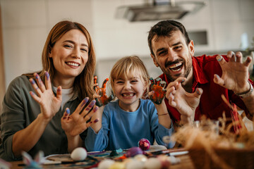 Portrait of a parents and daughter share laughter while decorating Easter eggs in the dining room