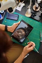 top view of repairman holding digital tablet with broken screen near other devices in workshop