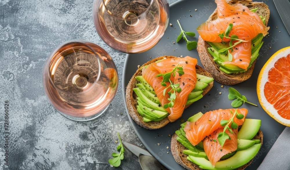 Wall mural avocado salmon toasts rose wine glasses and gray tabletop in top view for a gourmet lunch