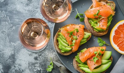 Avocado salmon toasts rose wine glasses and gray tabletop in top view for a gourmet lunch