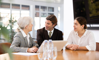 Adult man, elderly woman and young woman in business clothes having meeting in office