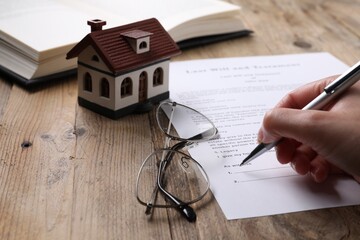Woman signing Last Will and Testament at wooden table, closeup