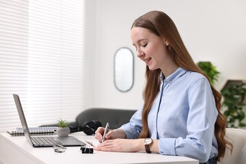 E-learning. Young woman taking notes during online lesson at white table indoors