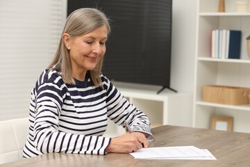 Senior woman signing Last Will and Testament at wooden table indoors. Space for text