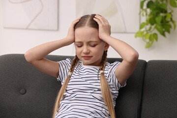 Little girl suffering from headache on sofa indoors