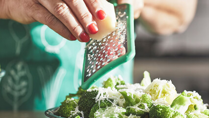 Closeup of a woman in apron grating cheese over salad.