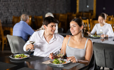 Couple of young man and woman having dinner and drinking wine together in restaurant