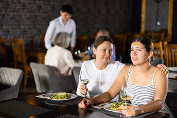 Young woman comforting upset female friend during friendly meeting over dinner in restaurant