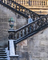A stylish Asian man in a light coat stands on ancient steps. Happy traveler looking at tourist...
