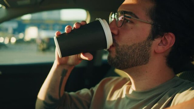 Young man driver close-up. Car sharing concept, vehicle and transport. Spanish happy guy driving, sitting in car and drinking coffee. Traveling by automobile.