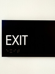 Black exit sign on a white wall with braille - 728871820