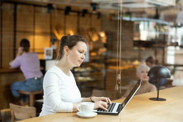 Middle-aged woman sitting at table, using laptop and enjoing cup of tea in coffee house. Modern female lifestyle concept