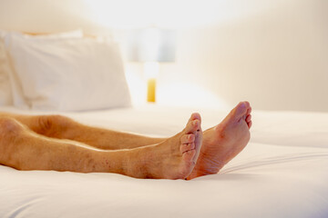 Selective focus of a men feet lied down on bed, Relaxing and watching TV on white bed sheet, A man...