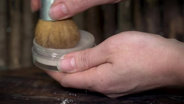 Woman checking natural loose powder in transparent container with make-up brash on wooden dark background.