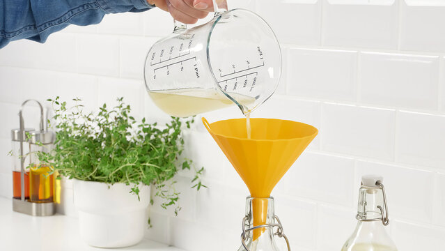 Closeup of man pouring lemonade in a bottle with a funnel.