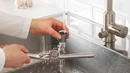 Man cleaning garlic crusher in kitchen sink.