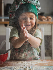 Cute toddler girl wearing toque playing with flour and clapping her hands. Defocused, vertical...