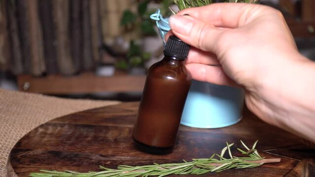 Women checking liquid cosmetic in glass amber bottle. Wooden background with fresh rosemary. Natural face and hair care.