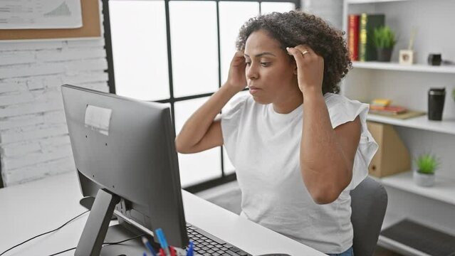 Black woman with curly hair working on computer in modern office.