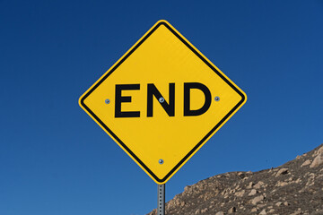Yellow And Black End Road Sign With Blue Sky And Rocky Hillside Behind